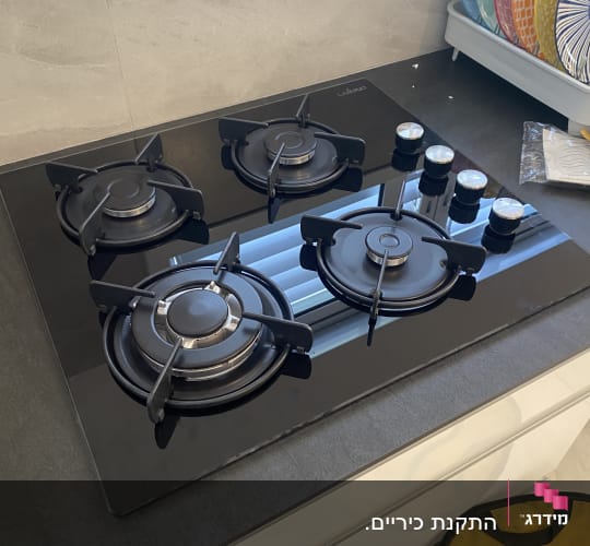 כיריים גז שחורות עם ארבעה מבערים וכפתורי שליטה
